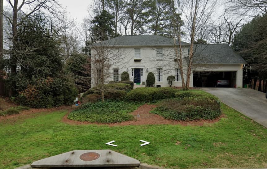 Two-story residential home with a manicured lawn and driveway, surrounded by trees.
