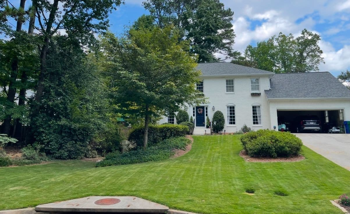 White suburban house with a manicured lawn, trees, and a garage on a sunny day.